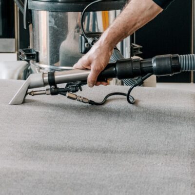 Osoba korzysta z odkurzacza do odświeżania tapicerki meblowej na szarym fotelu.