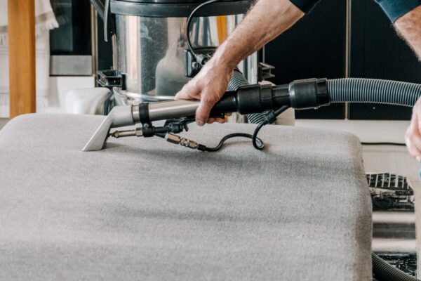 Osoba korzysta z odkurzacza do odświeżania tapicerki meblowej na szarym fotelu.